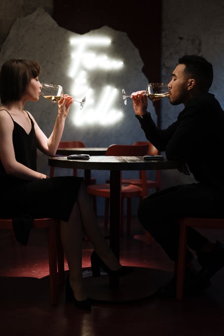 two people sitting at a table in a restaurant drinking wine